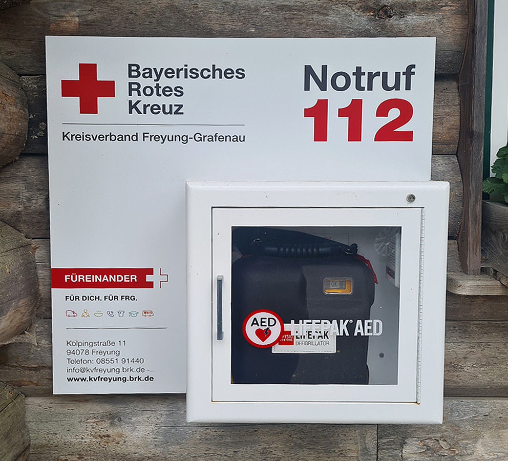 Öffentlich zugänglicher Defibrillator (AED) im Wandkasten mit Schild des BRK Kreisverbands Freyung-Grafenau und Notruf 112