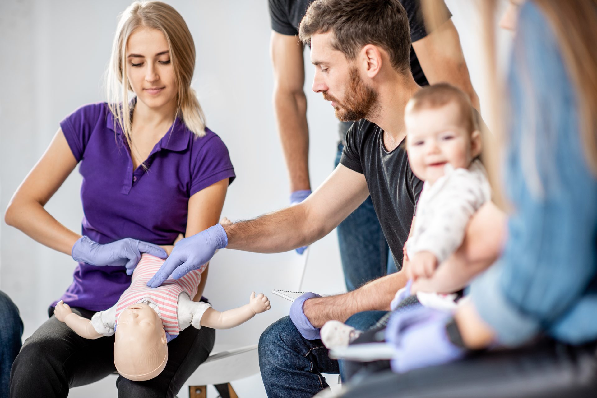 Eltern üben in einem Kurs an einer Babypuppe, ein Vater hält sein Baby auf dem Arm