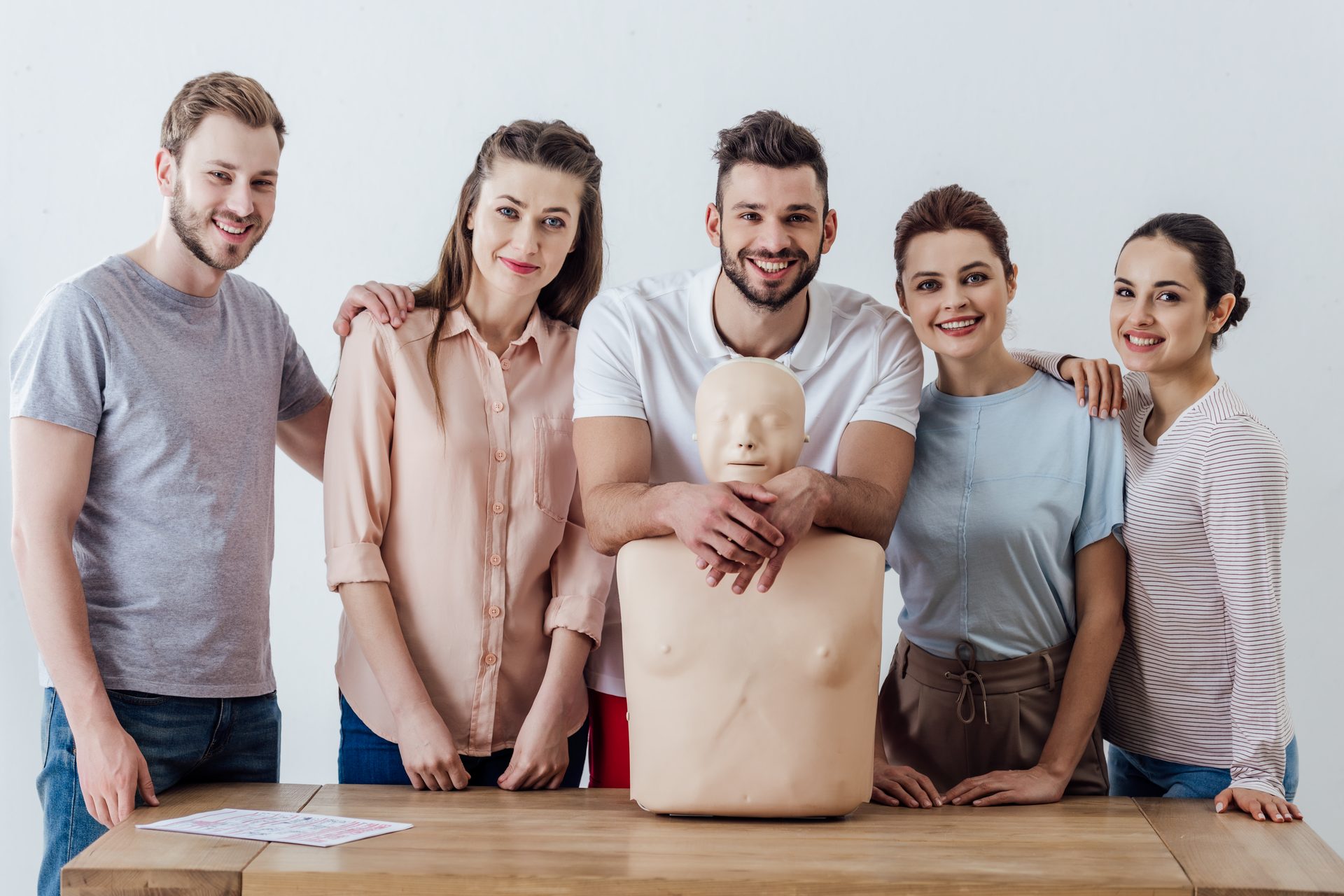 Eine Gruppe junger Erwachsener steht lächelnd um eine Übungspuppe