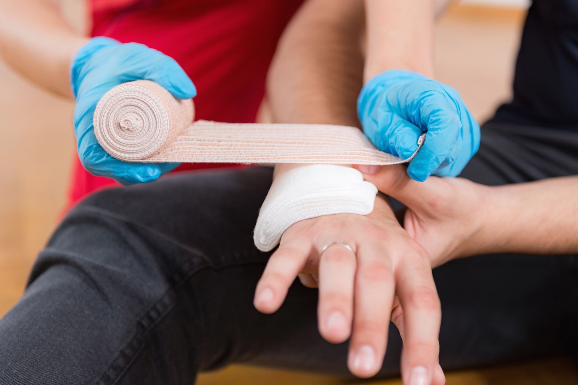 Hände in Einmalhandschuhen legen einen Verband an einer Hand an