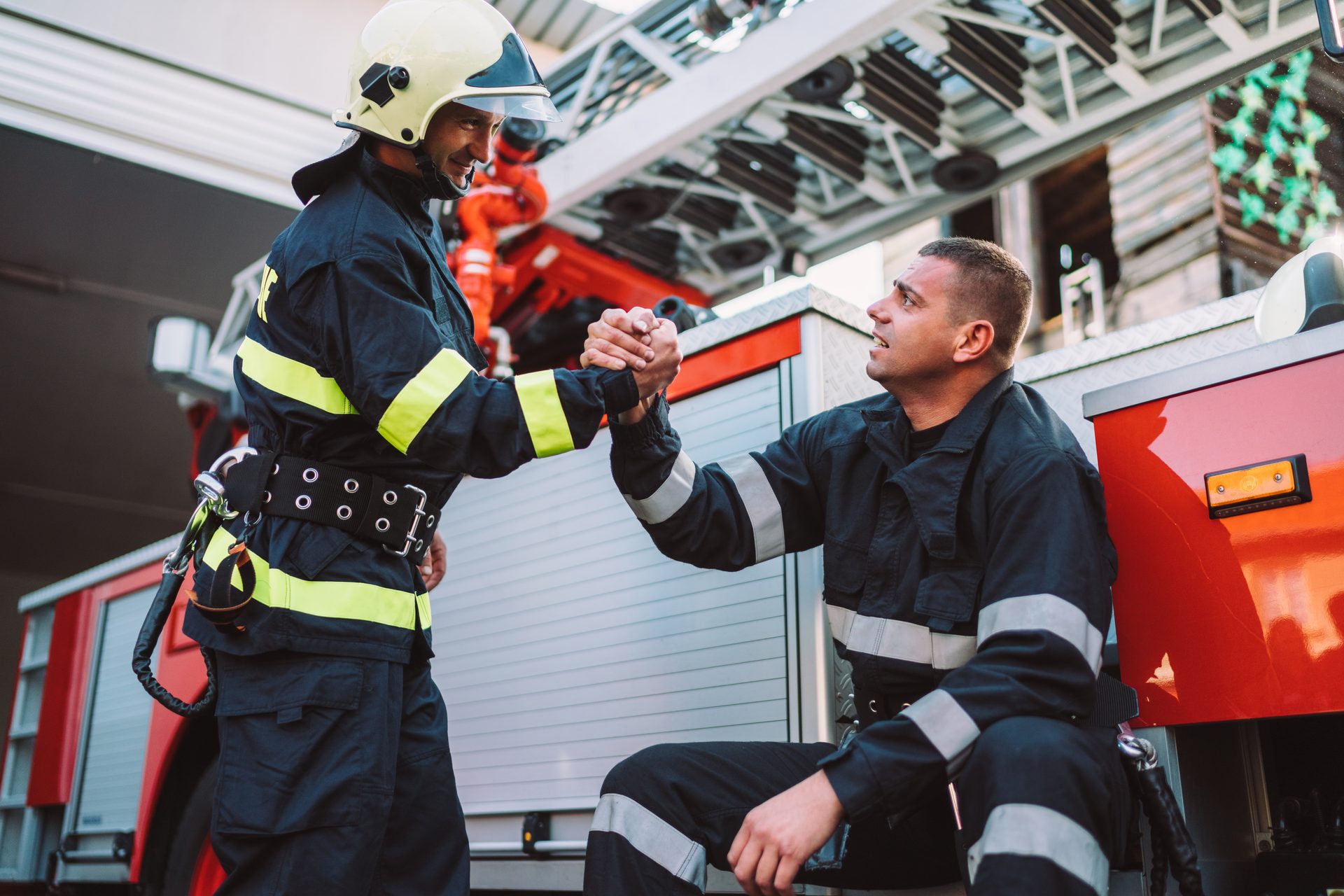 Zwei Feuerwehrleute reichen sich vor einem Einsatzfahrzeug die Hand