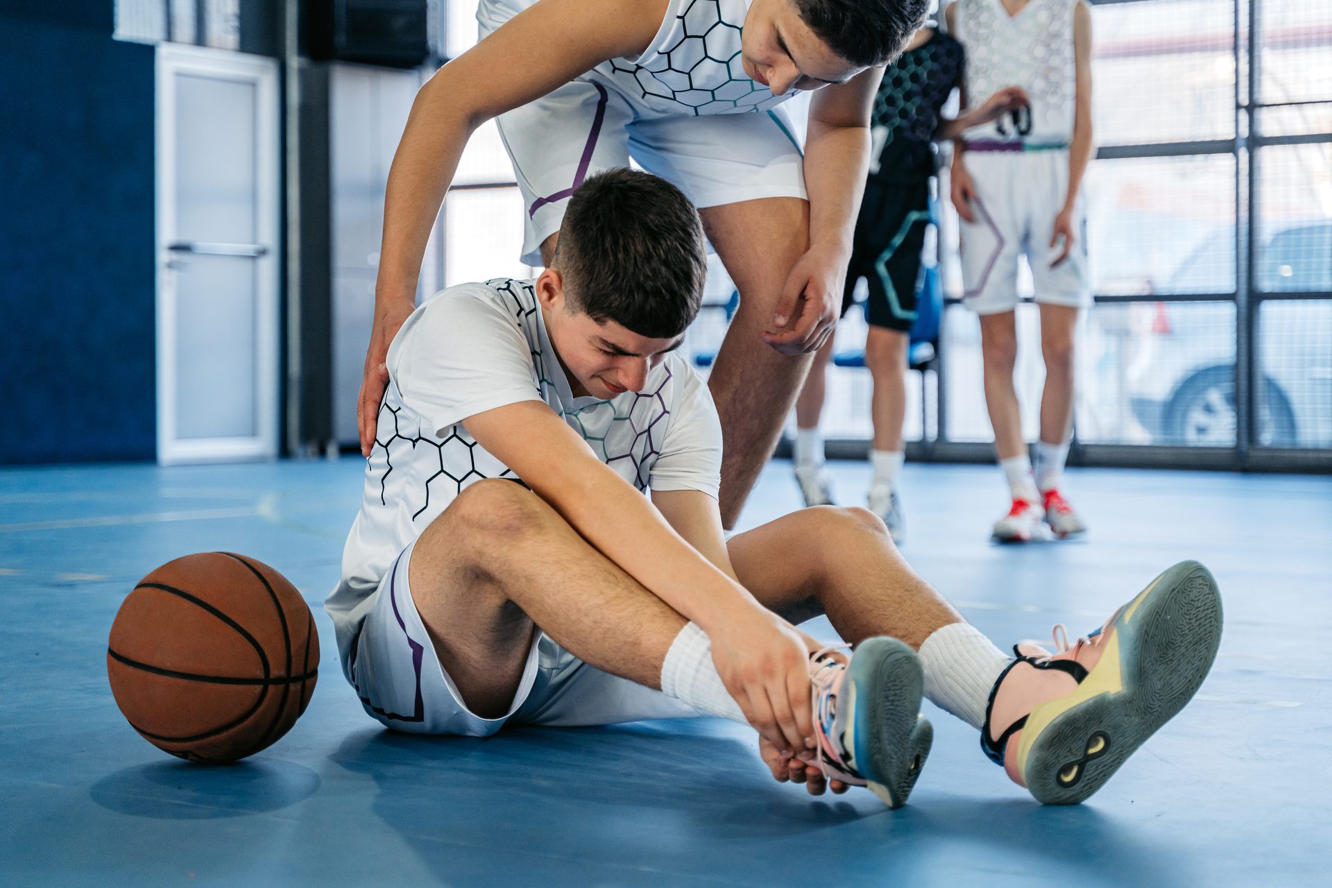 Ein Jugendlicher hilft einem Mitschüler, der sich in der Turnhalle am Knöchel verletzt hat