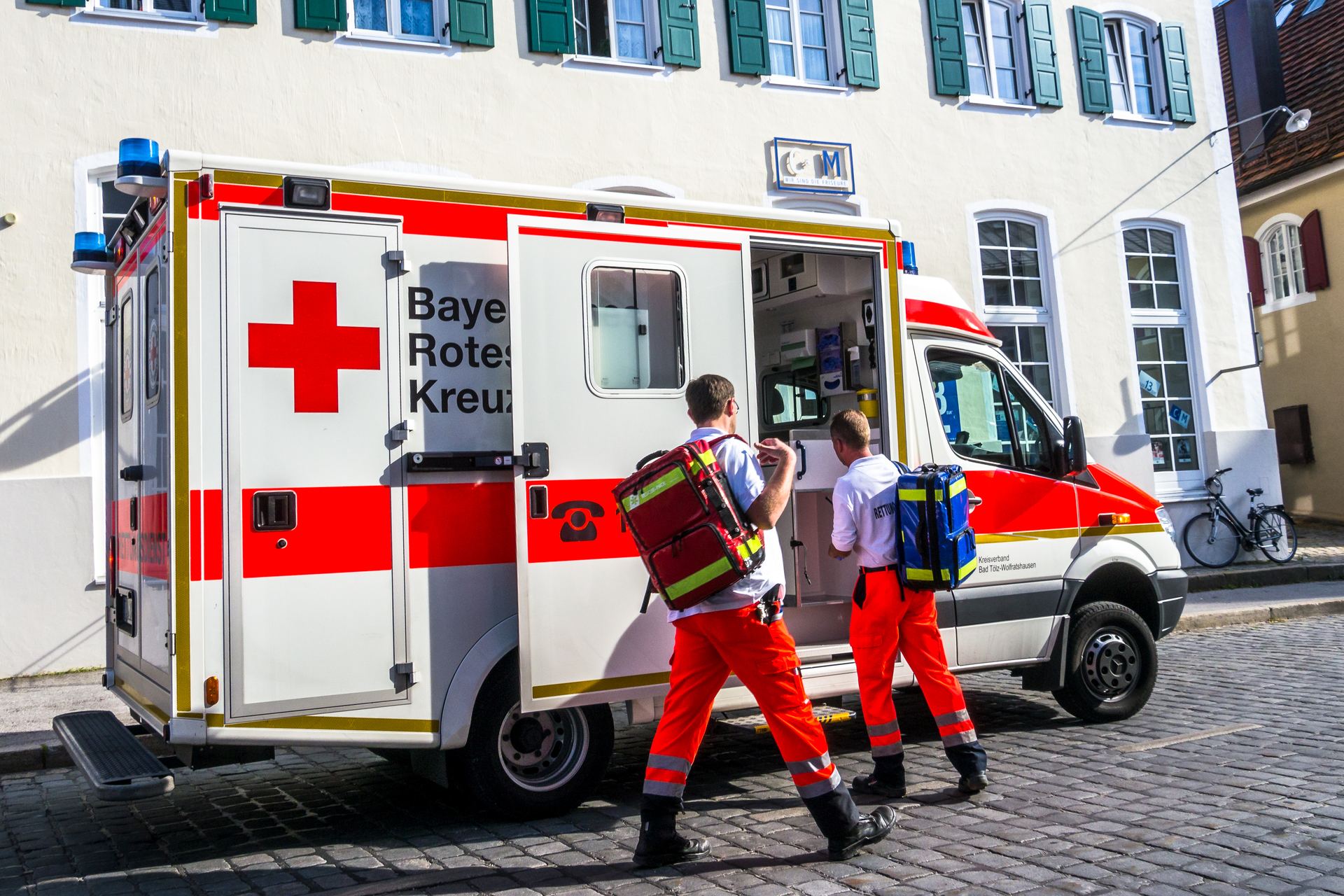 Zwei Rettungsdienstmitarbeiter tragen Notfallrucksäcke zum geöffneten Rettungswagen