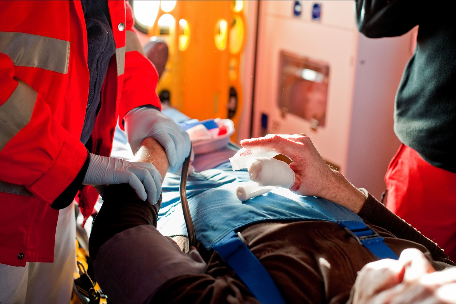 Helfer in Einsatzkleidung versorgen einen Patienten auf der Trage, seine Hand ist verbunden