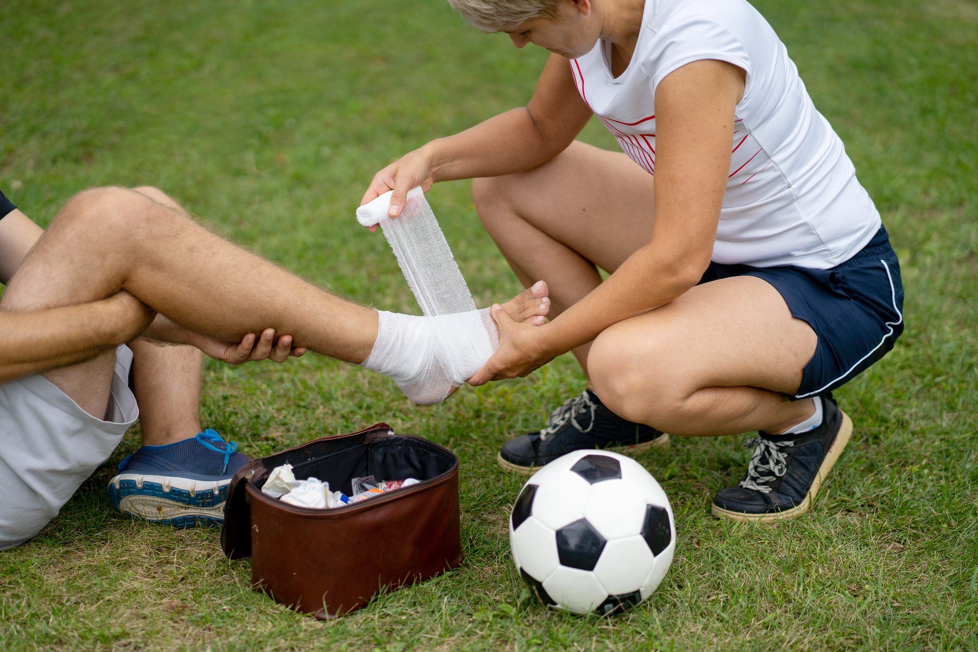 Eine Trainerin verbindet am Spielfeldrand den Knöchel eines Fußballers
